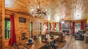 L’intérieur d’un chalet en bois comprend une table à manger, des chaises, une cheminée et un ventilateur de plafond.