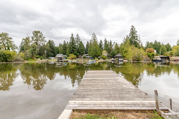 A wooden dock extending into calm water with reflections of surrounding trees and buildings. - Lakefront Cottage Near Crystal Mountain & Rainier (Sumner)