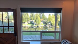 A room with a large window overlooking a backyard with a wooden deck, a chair, and a small table. - Lakefront Cottage Near Crystal Mountain & Rainier (Sumner)