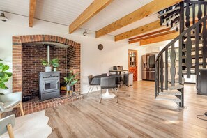 Une cuisine moderne avec une cheminée en briques, un coin repas avec une table et des chaises, et un escalier en bois.