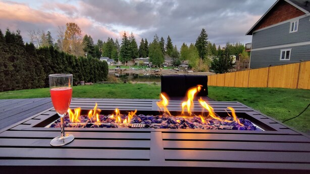 A backyard with a fire pit, a glass of red drink, and a view of a neighborhood. - Lakefront Cottage Near Crystal Mountain & Rainier (Sumner)