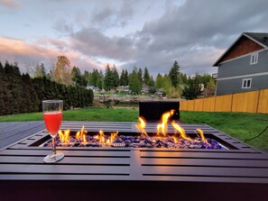 A backyard with a fire pit, a glass of red drink, and a view of a neighborhood. - Lakefront Cottage Near Crystal Mountain & Rainier (Sumner)