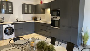 A modern kitchen with dark cabinetry, a built-in washing machine, and a dining area with a table set for two.