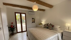 A bedroom with a bed, nightstands, a lamp, a potted plant, and a door leading to an outdoor area.