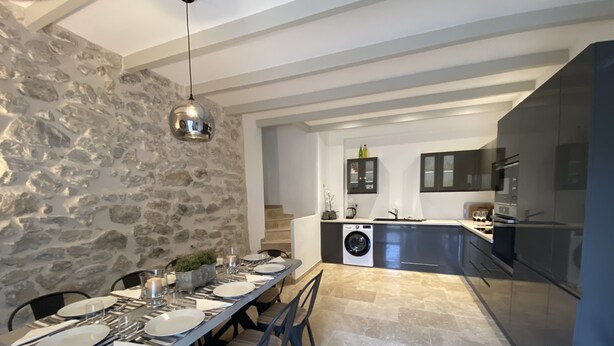 A modern kitchen with a stone wall, a built-in washing machine, and a dining area with a long table and chairs.
