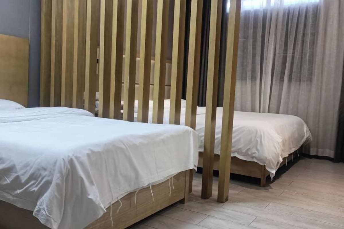 A hotel room with two beds, a wooden partition, and a view of a building through sheer curtains.