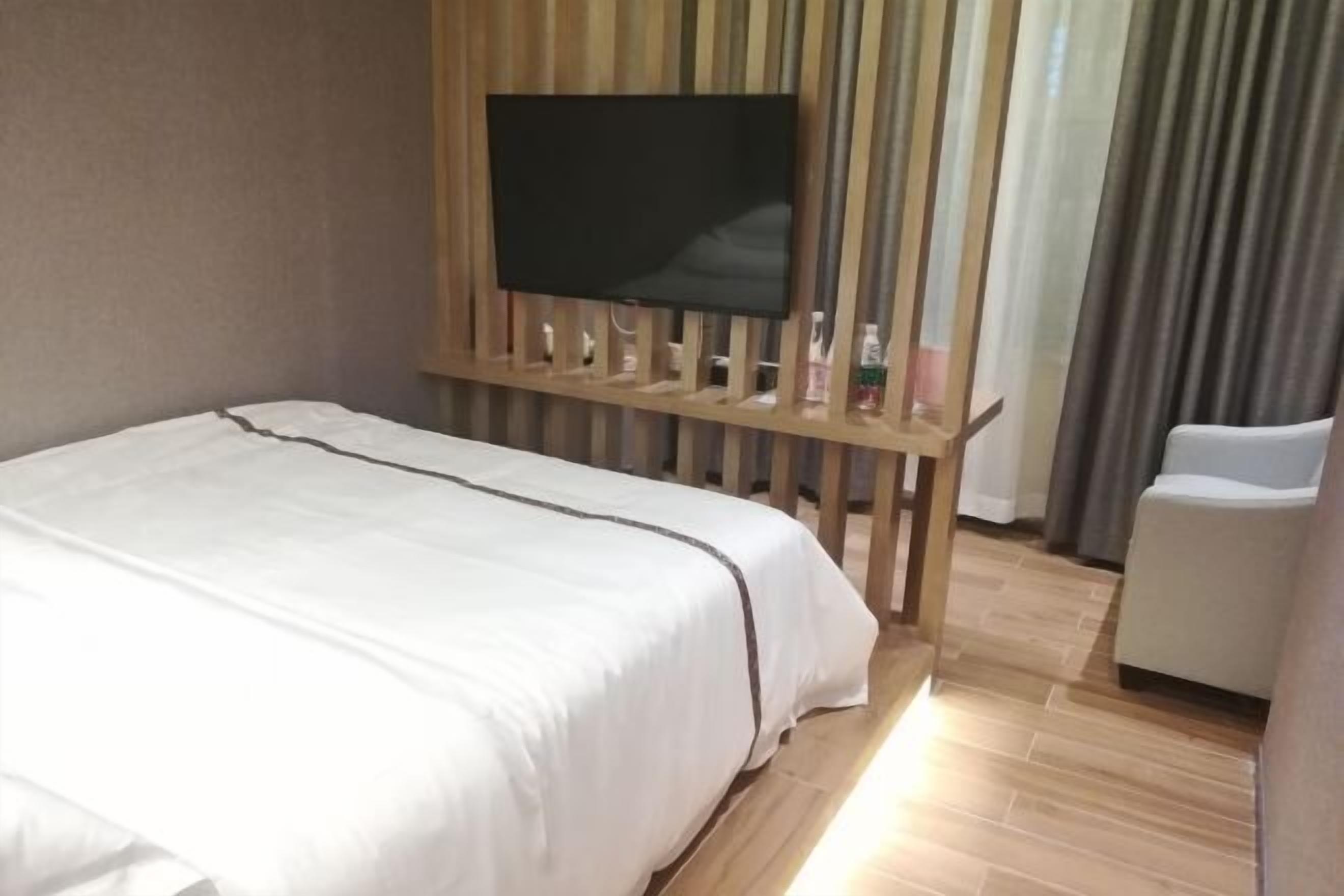 Ein Hotelzimmer mit Bett, Fernseher an einer Holzverkleidung, Sessel und Vorhang.