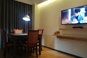 Een kamer met een eettafel, stoelen, een aan de muur bevestigde televisie en een klein plankje met spullen.