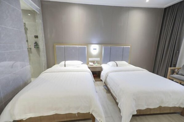 Habitación de hotel con dos camas, un espejo, una mesita de noche y una zona de ducha.