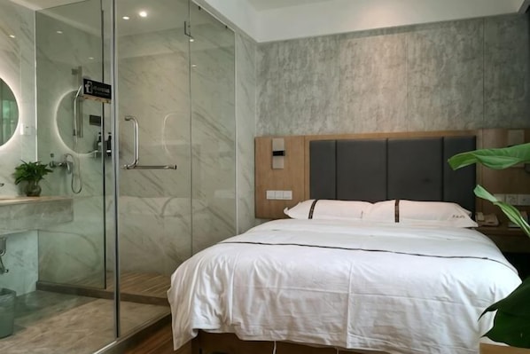 A modern hotel room with a glass-enclosed shower, a large bed with white bedding, a wooden headboard, and a marble wall. - Jinqiao Hotel (Shenzhen Longhua) (Shenzhen)
