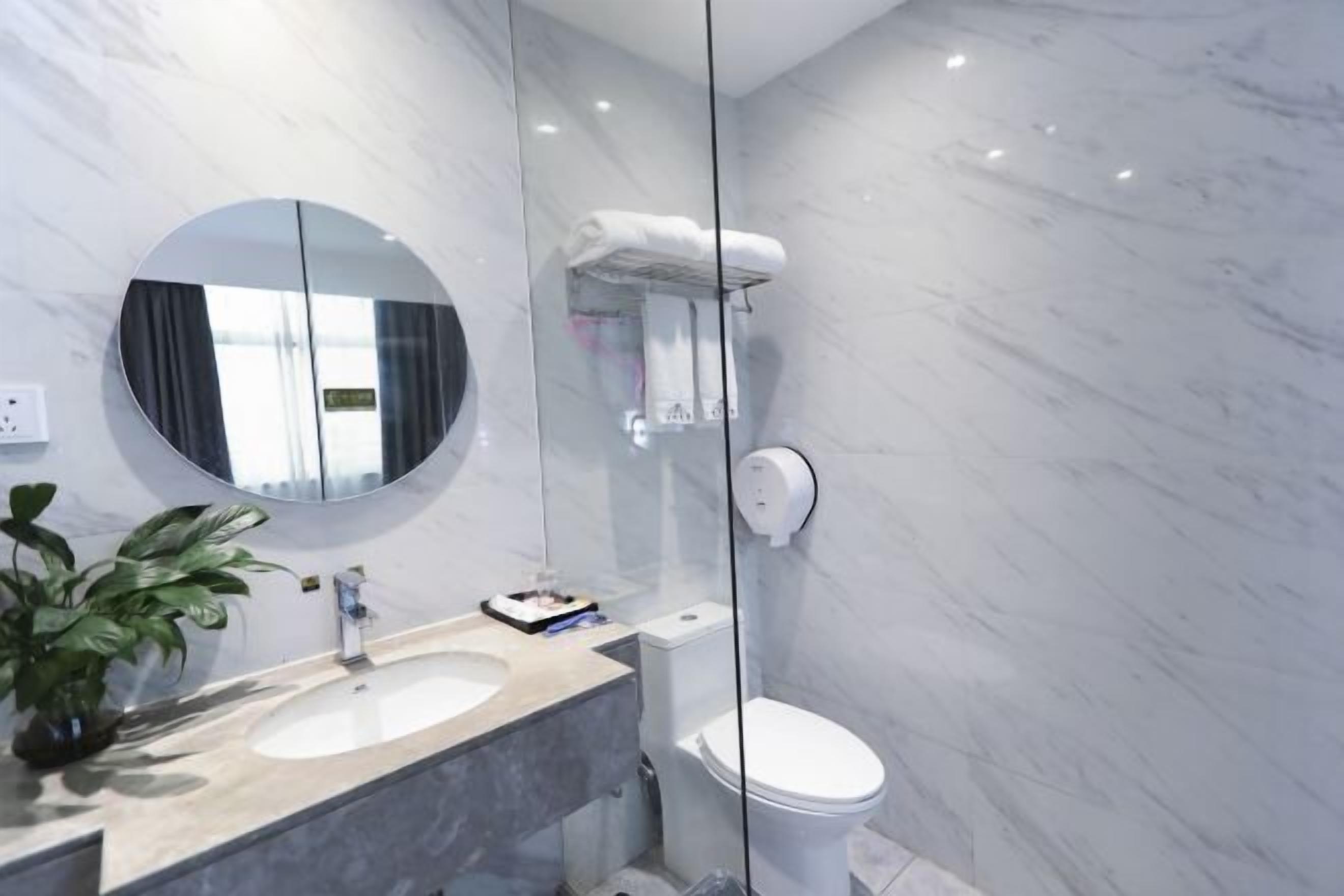 A modern bathroom with a marble sink, a round mirror, a toilet, and a glass shower enclosure.