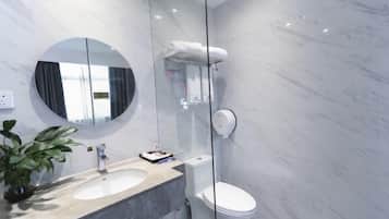 A modern bathroom with a marble sink, a round mirror, a toilet, and a glass shower enclosure.