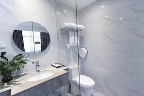 A modern bathroom with a marble sink, a round mirror, a toilet, and a glass shower enclosure. - Jinqiao Hotel (Shenzhen Longhua) (Shenzhen)