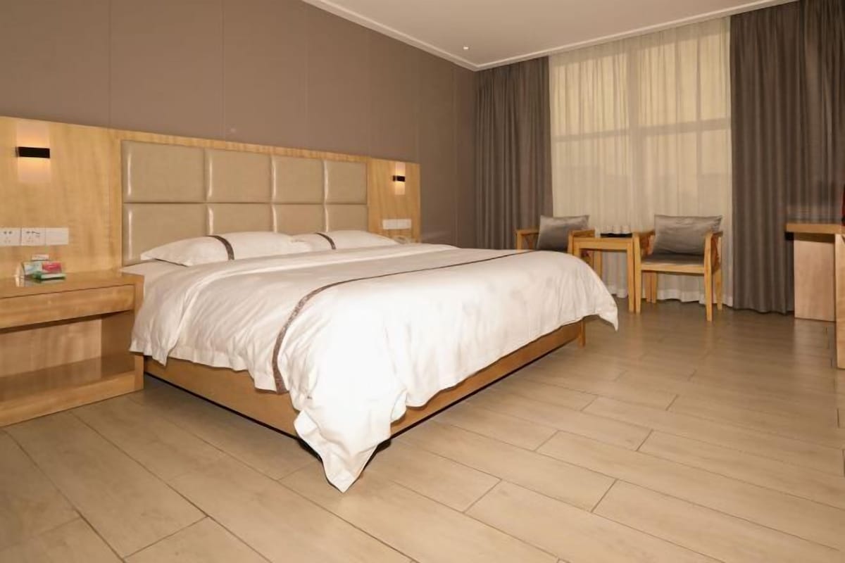 A modern hotel room with a large bed, wooden headboard, and a small desk with a chair.