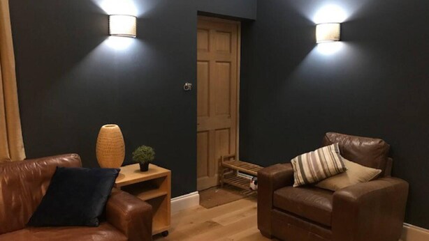 A dark-colored room with two leather sofas, a small wooden table, and two wall-mounted lights. - Lovely and Comfortable 1-bed Apartment in Bromley (Bromley)
