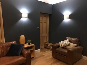 A dark-colored room with two leather sofas, a small wooden table, and two wall-mounted lights. - Lovely and Comfortable 1-bed Apartment in Bromley (Bromley)