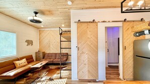 A cozy room with a wooden ceiling, a brown leather sofa, a wooden dining table, and a sliding barn door. - NEWTinycabin/Hottub/Firepit/Yard/5minParkWay (Sevier County)
