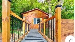 A wooden cabin with a porch and a metal railing, surrounded by greenery. - NEWTinycabin/Hottub/Firepit/Yard/5minParkWay (Sevier County)