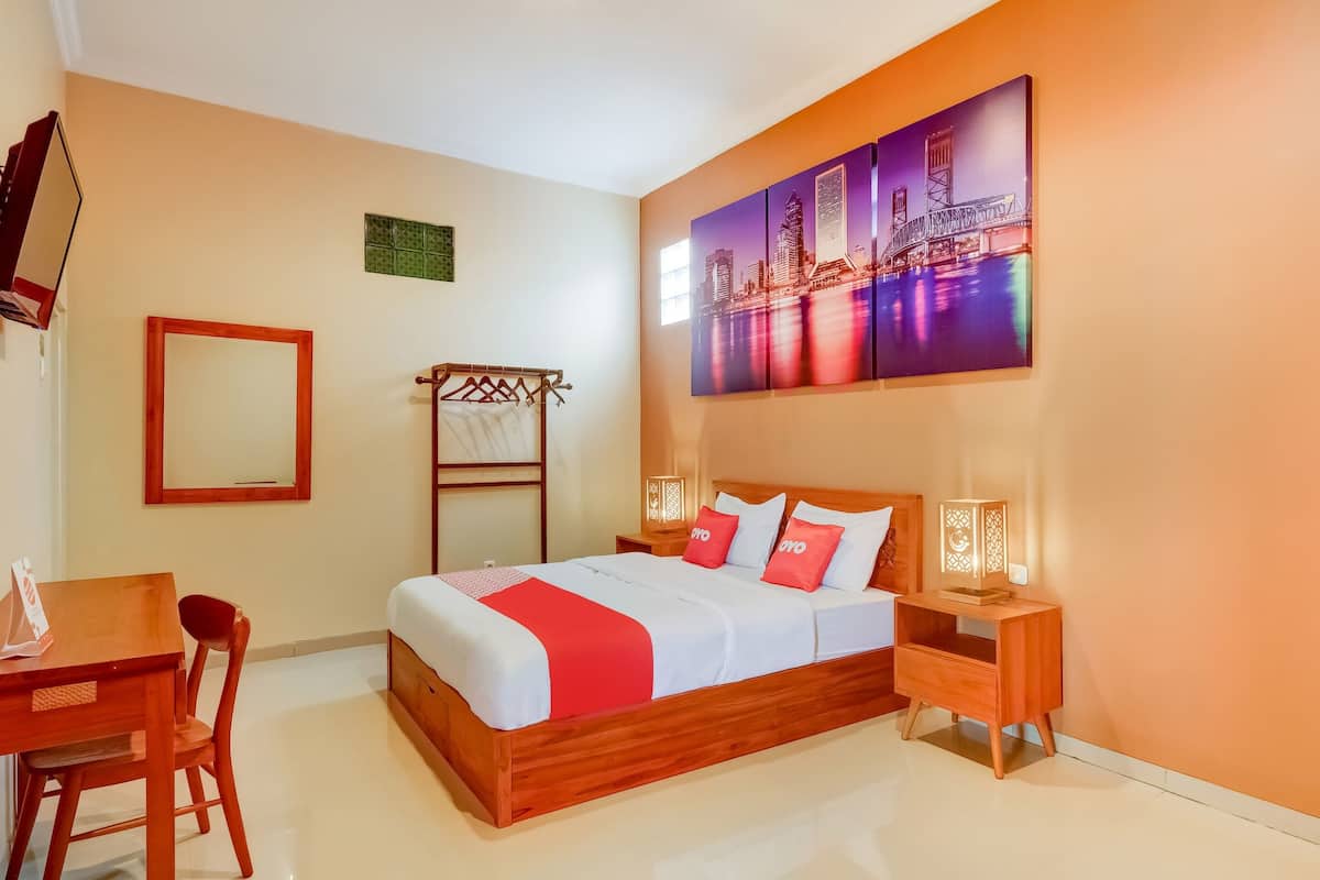 A hotel room with a wooden bed, a cityscape painting, a wooden nightstand, and a desk with a chair.