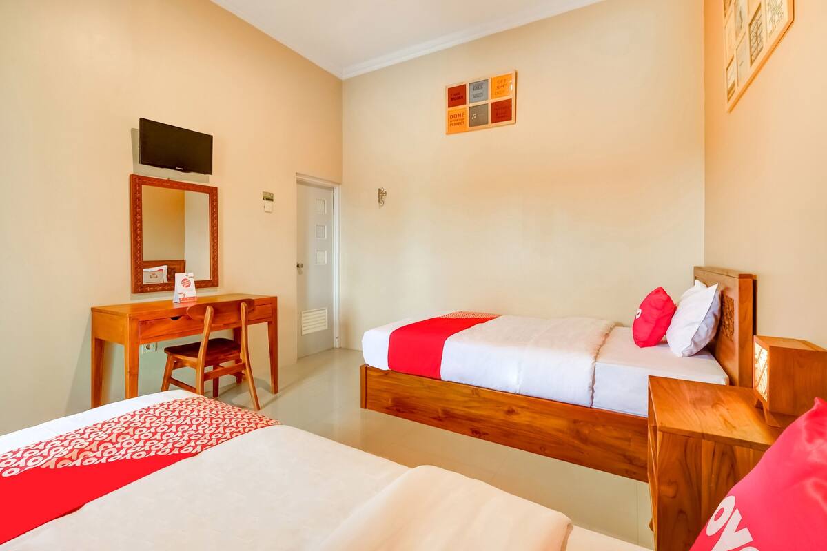 A hotel room with two beds, a desk, a chair, a television, and a door.