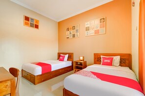 Habitación de hotel con dos camas, cada una con cabecero de madera y colcha blanca y roja. Hay dos mesitas de noche con lámparas, y las paredes están decoradas con cuadros enmarcados.