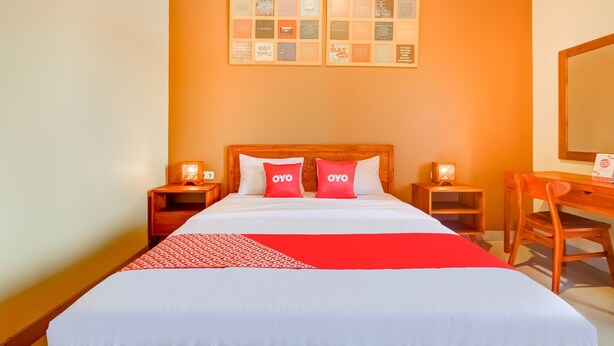 A hotel room with a large bed, two bedside tables with lamps, a wooden desk, and a wall with framed pictures. - Griya Gayatri Syariah (Ngaglik)