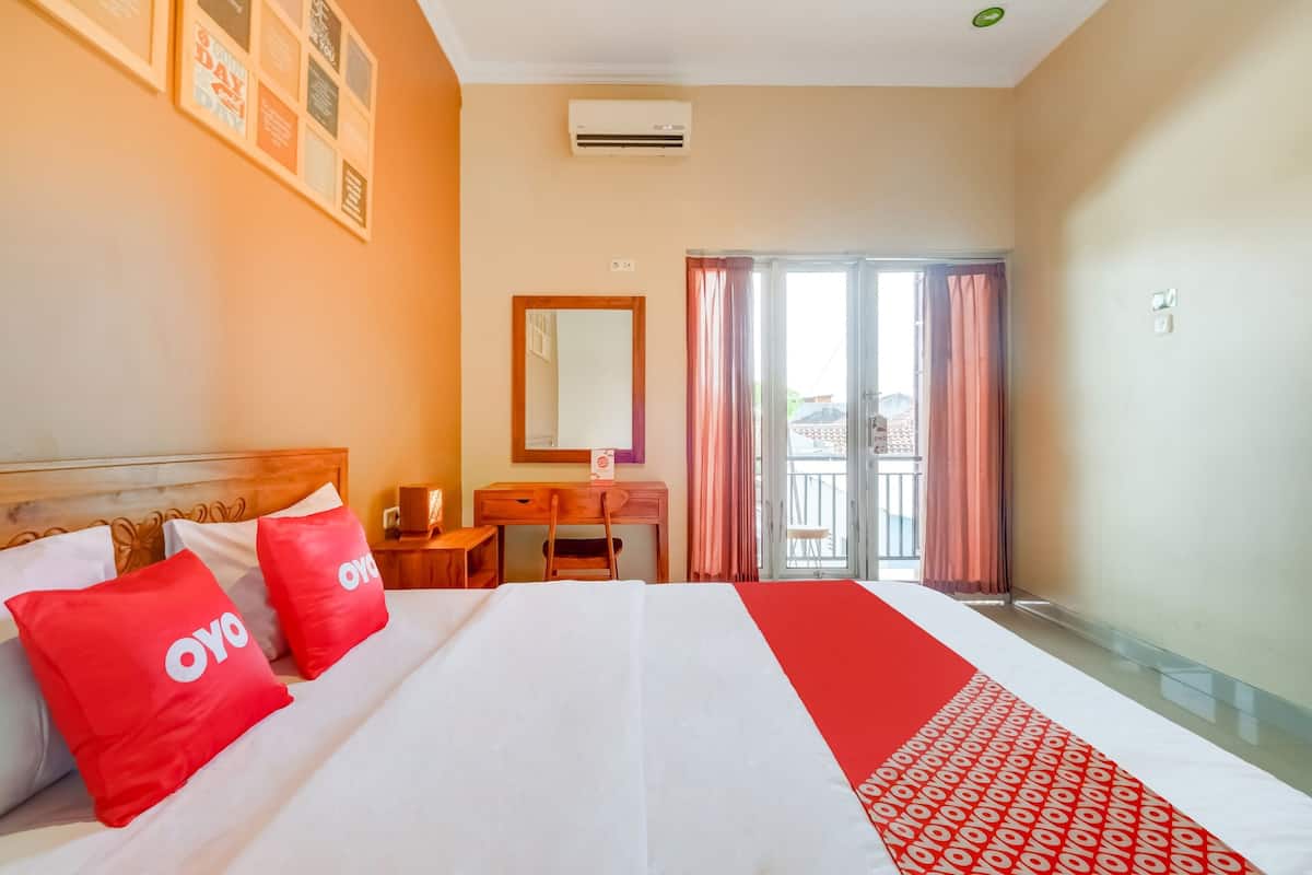 A hotel room with a bed, a desk, a chair, a mirror, and a sliding glass door leading to an outdoor area.