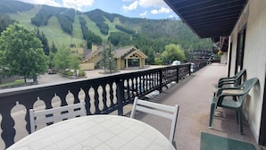 A balcony with a view of a mountain landscape, a wooden building, and a parking area.