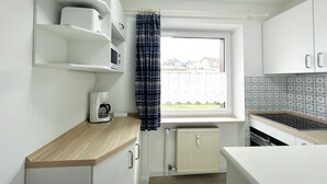 A compact kitchen with white cabinets, a wooden countertop, a built-in microwave, and a window with a view of houses. - Klaus-Groth-Str 2 App 11 Westerland (Westerland)
