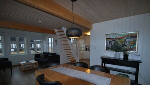 Amplia sala de estar con una mesa de comedor de madera, sillas negras y una escalera que conduce a un nivel superior.
