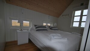 Un dormitorio con techo de madera, paredes blancas, una cama con almohadas a rayas, una mesita de noche con lámpara y una ventana con vistas.