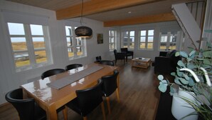 Un comedor espacioso con una mesa y sillas de madera, ventanas amplias con vistas al exterior y una escalera que sube a un nivel superior.