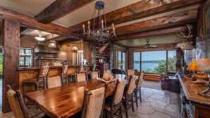 A rustic dining area with a large wooden table and chairs, a chandelier, and a view of the outdoors. - PRIVATE 10,000 SqFt lakefront log estate  w. Pool  - Golfers Retreat - Close to Big Cedar! (kirbyville)