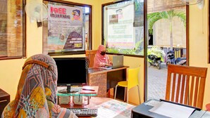 A reception desk with a computer, a printer, and a window with a view of the street and parked motorcycles. - OYO 90065 Homestay Barokah Park (Asembagus)