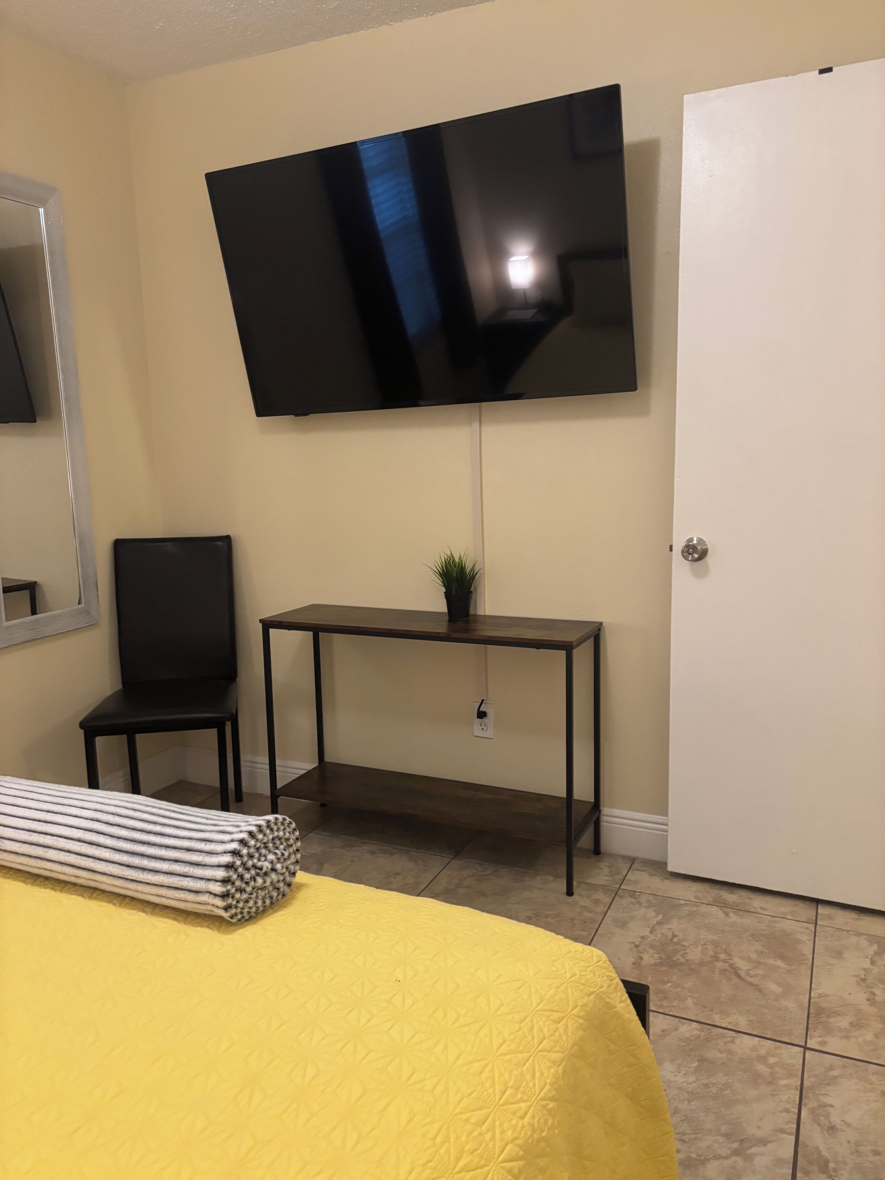 Een kamer met een bed, een bureau, een stoel, een aan de muur bevestigde televisie en een deur.