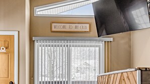 A modern interior with a wooden ceiling, a flat-screen TV mounted on the wall, a sliding glass door leading to a balcony, and a welcome sign.