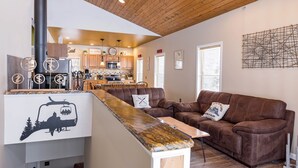 A cozy living area with a brown leather sofa, a wooden coffee table, and a kitchen in the background.