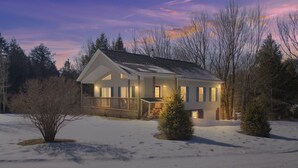 A two-story house with a covered porch, surrounded by snow and trees.