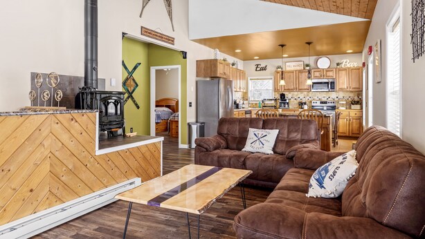 A spacious living area with a fireplace, a sofa, and a coffee table. A kitchen with wooden cabinets and a dining area is visible in the background.