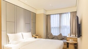 A modern hotel room with a large bed, a bedside table, a small desk with a chair, a TV, and a window with curtains. - Ji Hotel Shanghai The Bund Town City God Templ (Shanghai)