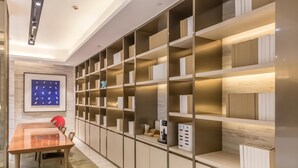 A modern room with a long wooden table, chairs, and built-in shelving with books and a coffee machine. - Ji Hotel Shanghai The Bund Town City God Templ (Shanghai)