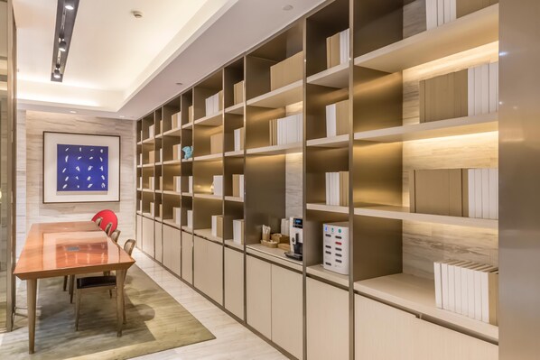 A modern room with a long wooden table, chairs, and built-in shelving with books and a coffee machine. - Ji Hotel Shanghai The Bund Town City God Templ (Shanghai)