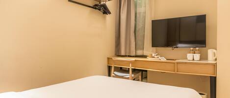 A hotel room with a bed, a desk, a flat-screen TV, a coffee maker, and a window with curtains.