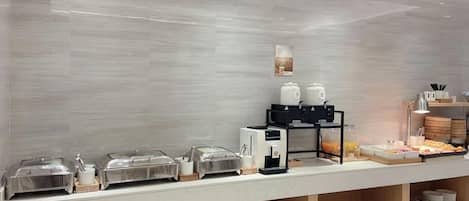 A buffet setup with various food containers and a coffee machine.