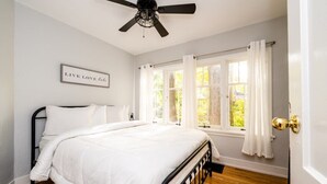 Un dormitorio con cama, ventilador de techo, ventana con cortinas y un cartel en la pared.
