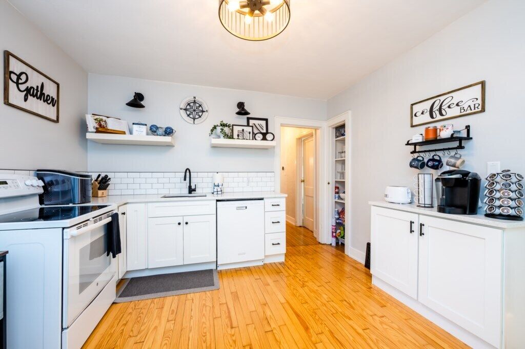 A modern kitchen with white cabinetry, a built-in oven, a microwave, and a coffee bar with mugs and a coffee machine.