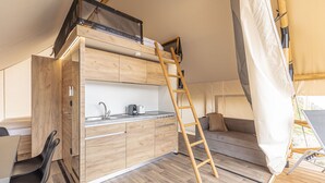 Una kitchenette moderna y compacta con encimera de madera, un lavamanos y una estufa. Una escalera de madera da acceso a una zona de dormitorio en altura.
