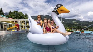 A group of people on a swan-shaped inflatable in a pool with a mountain backdrop.