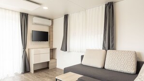 Habitació moderna i ben il·luminada amb un sofà gris, una taula de fusta petita i un televisor fixat a la paret.