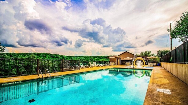 Una piscina con lettini e una zona coperta, circondata da una recinzione e alberi.